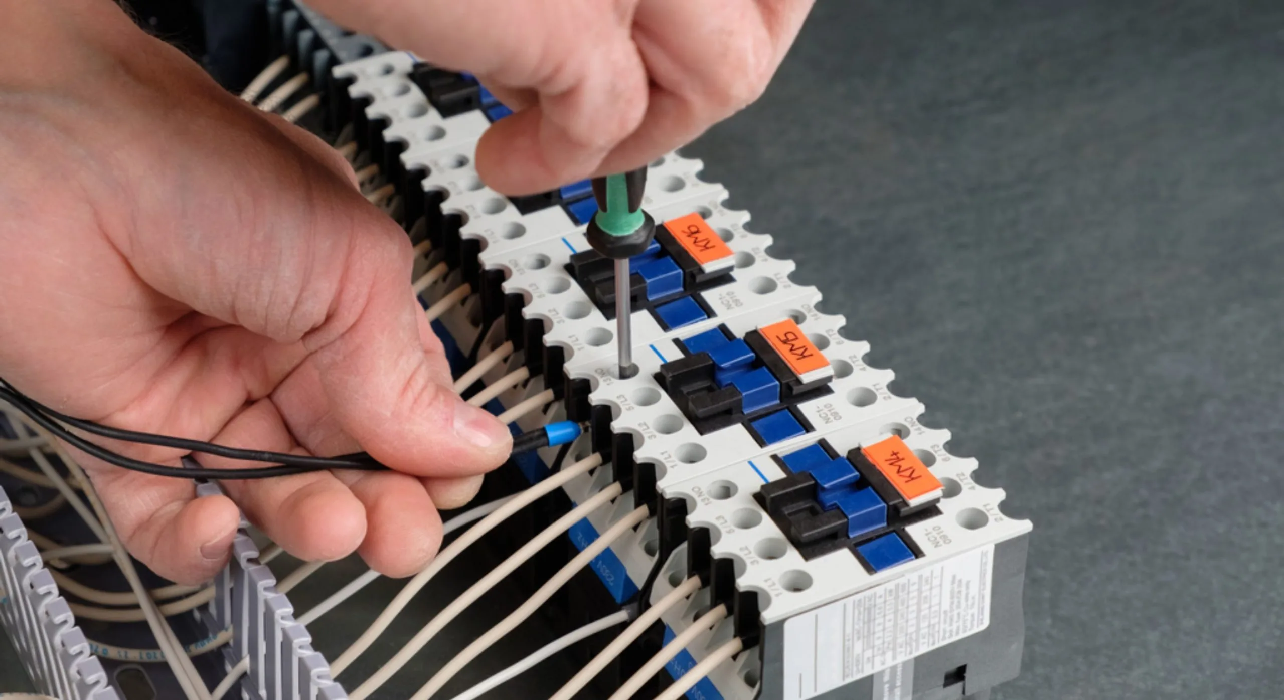 Electrician using a screwdriver to secure connections on an industrial terminal block