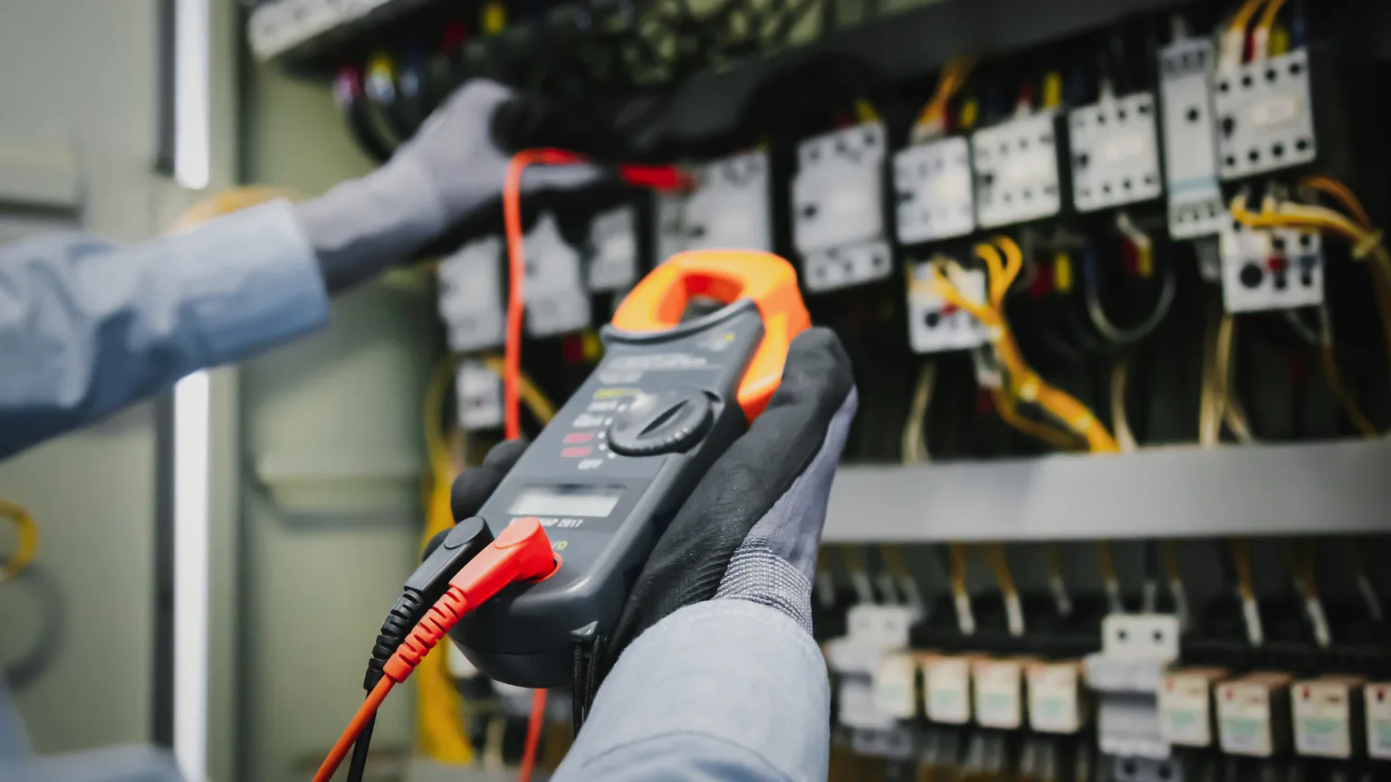 A person in gloves checks electrical connections using a multimeter