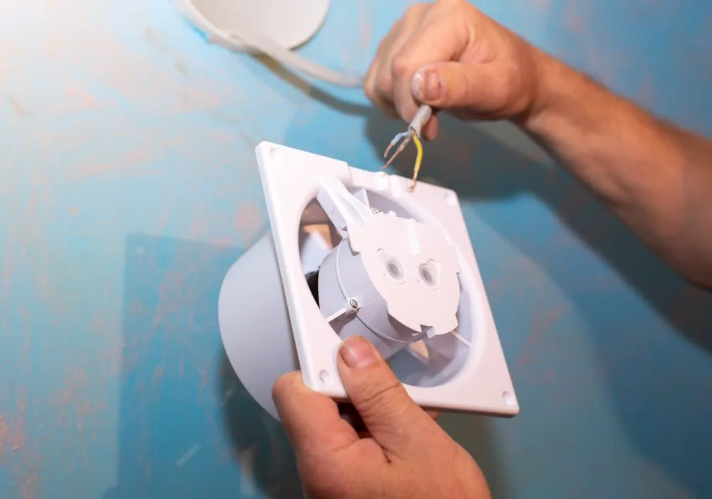 A person is installing a ventilation fan onto a blue wall