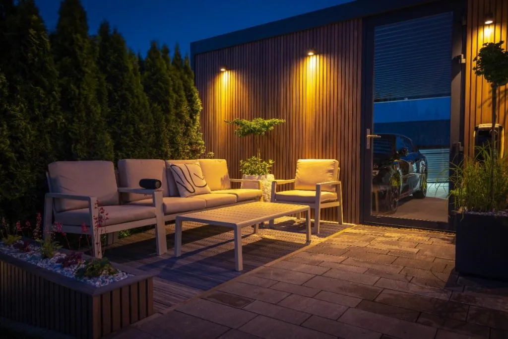 Soft, warm lighting illuminates a cozy patio with comfortable seating amid greenery