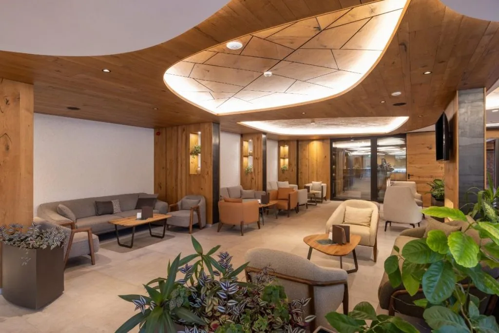 A modern lounge features warm wood accents, comfortable seating, and lush greenery