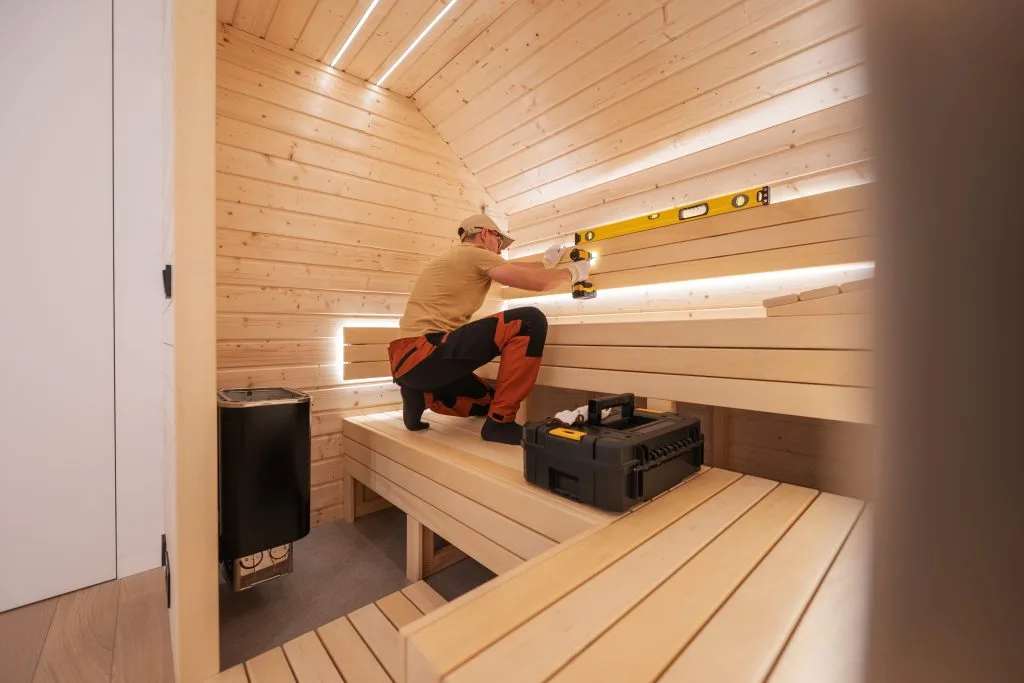 A worker installs wooden benches in a cozy, lit sauna