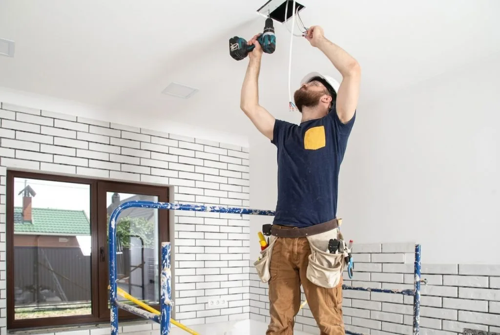 Electrician Airdrie installs ceiling fixtures using a power tool for efficient lighting solutions