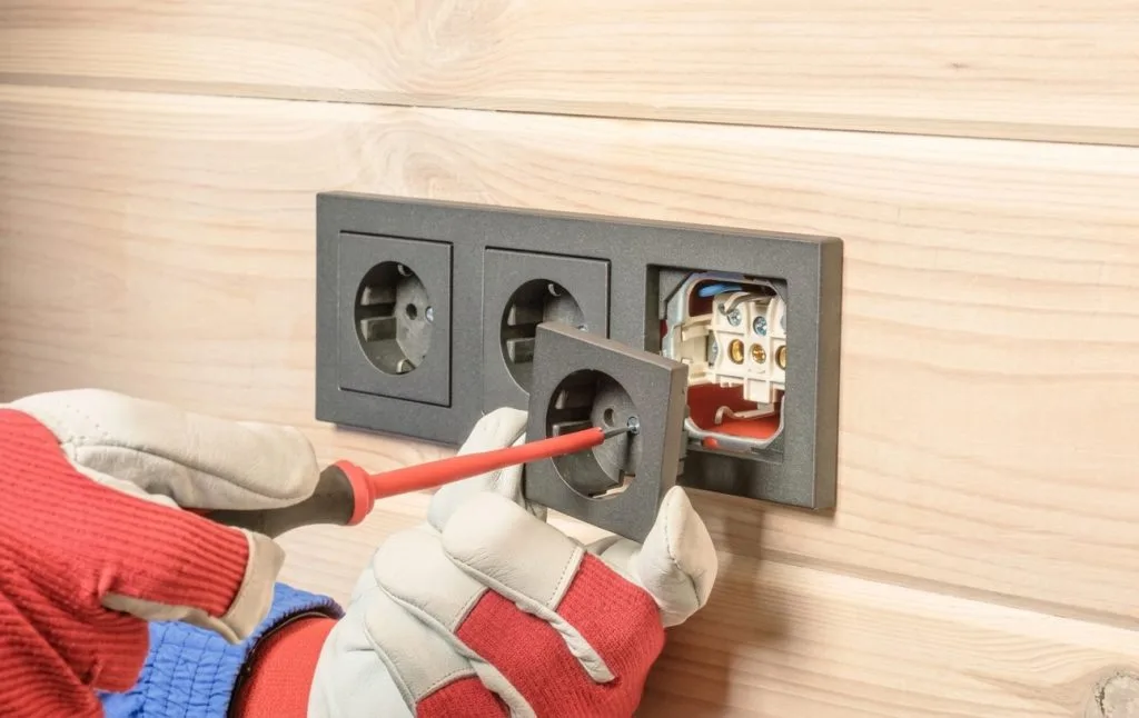 Electrician Airdrie installing an electrical outlet with a screwdriver